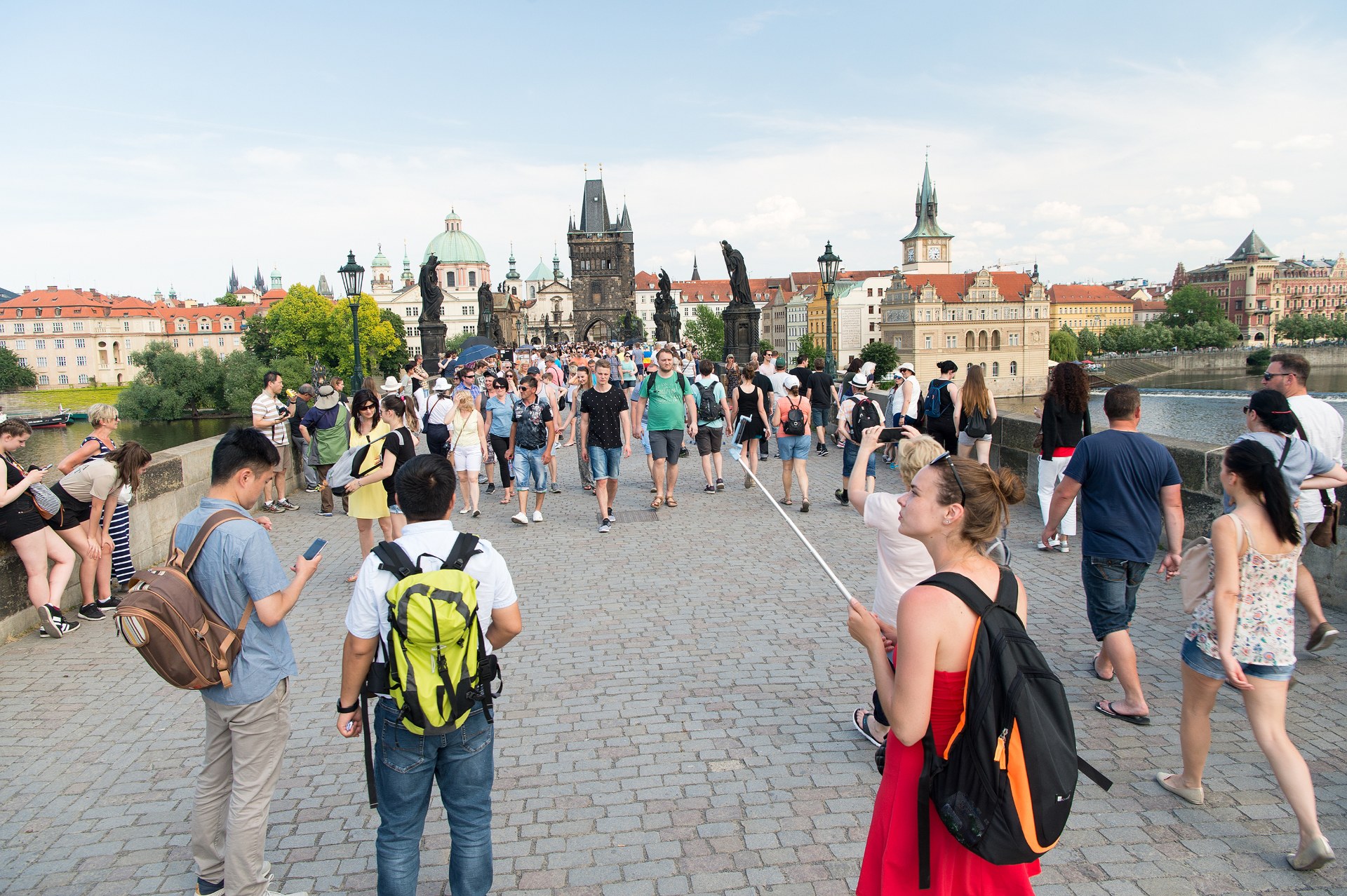Young people with backpacks walking across Charles Bridge in Prague with the Old Town bridge tower behind
